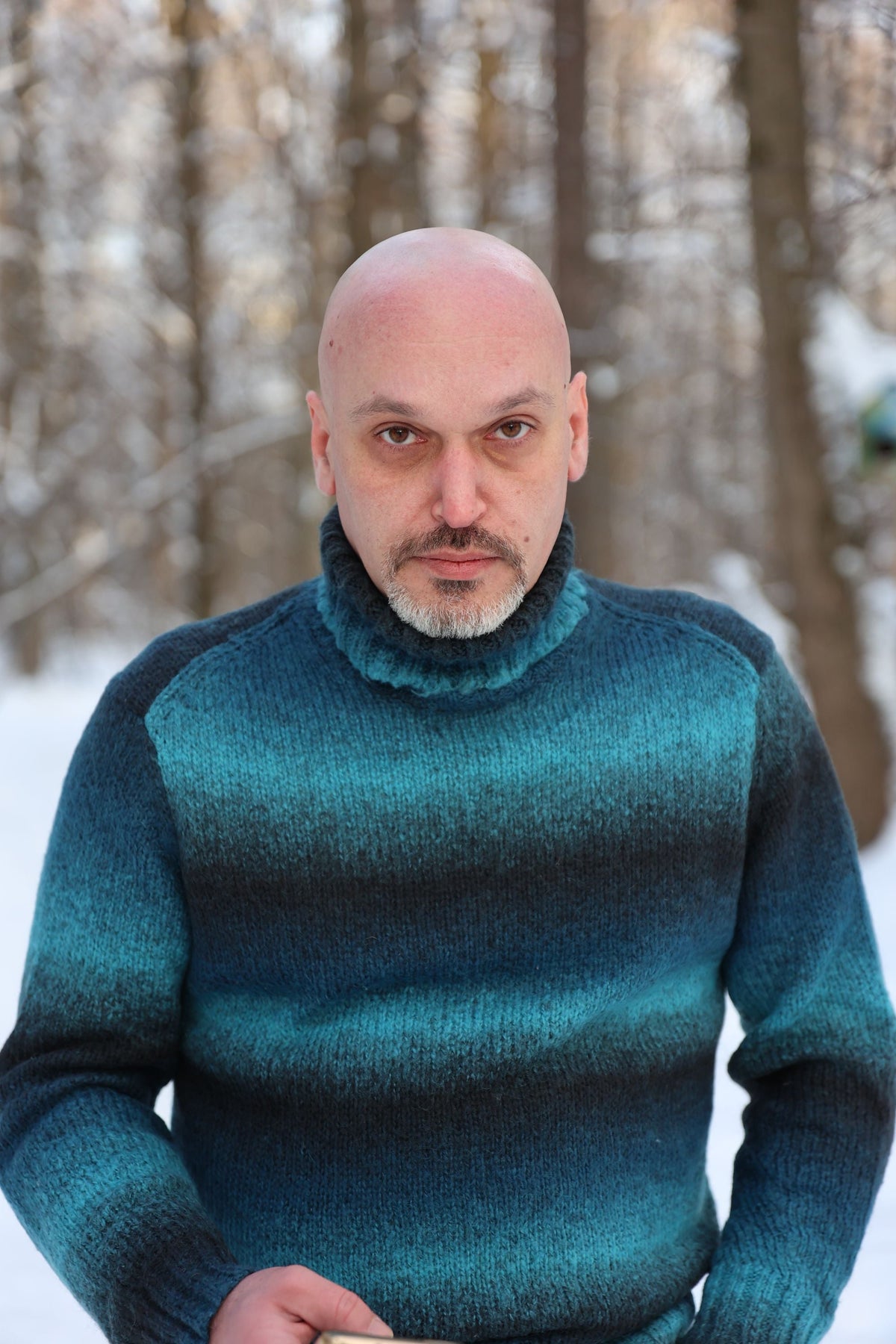 Man wearing a teal knit turtleneck sweater standing outdoors in a snowy forest