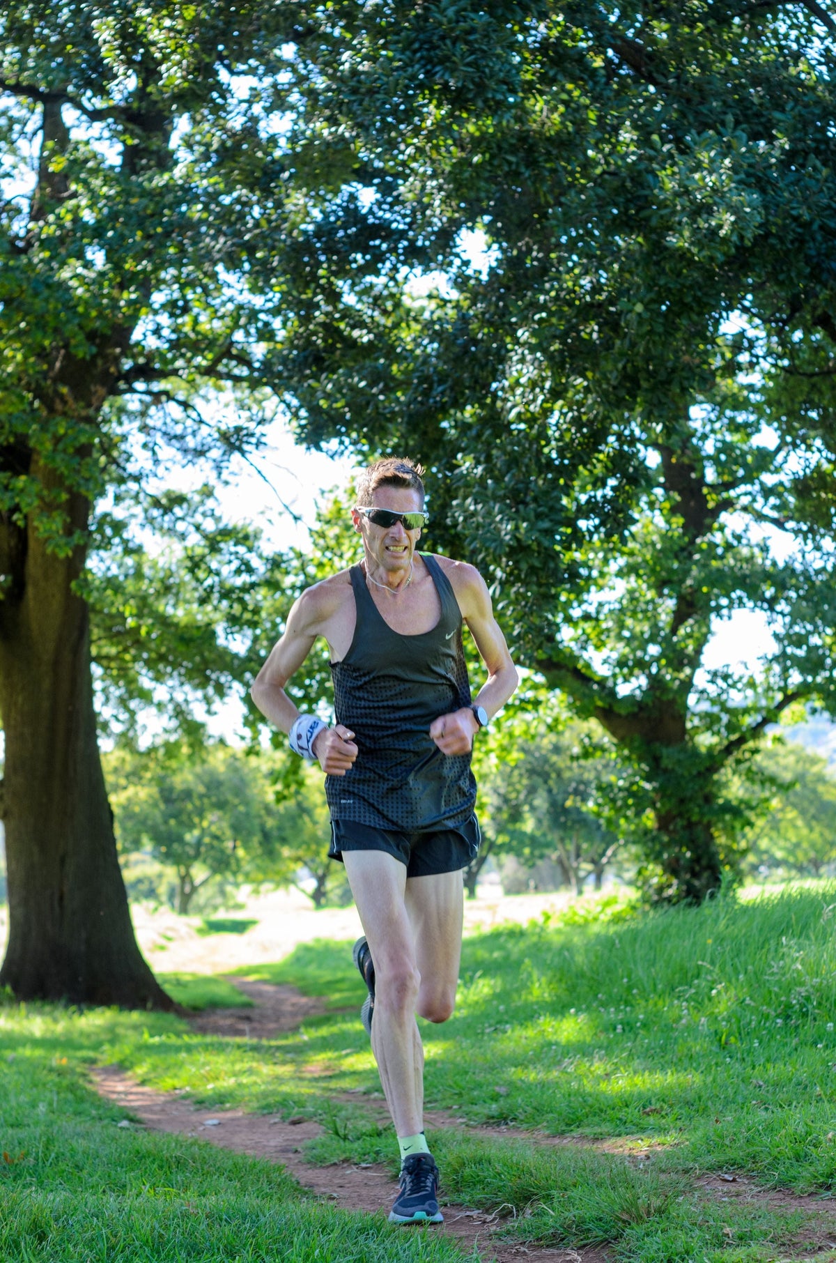 Man wearing athletic tank top and shorts running on a wooded trail