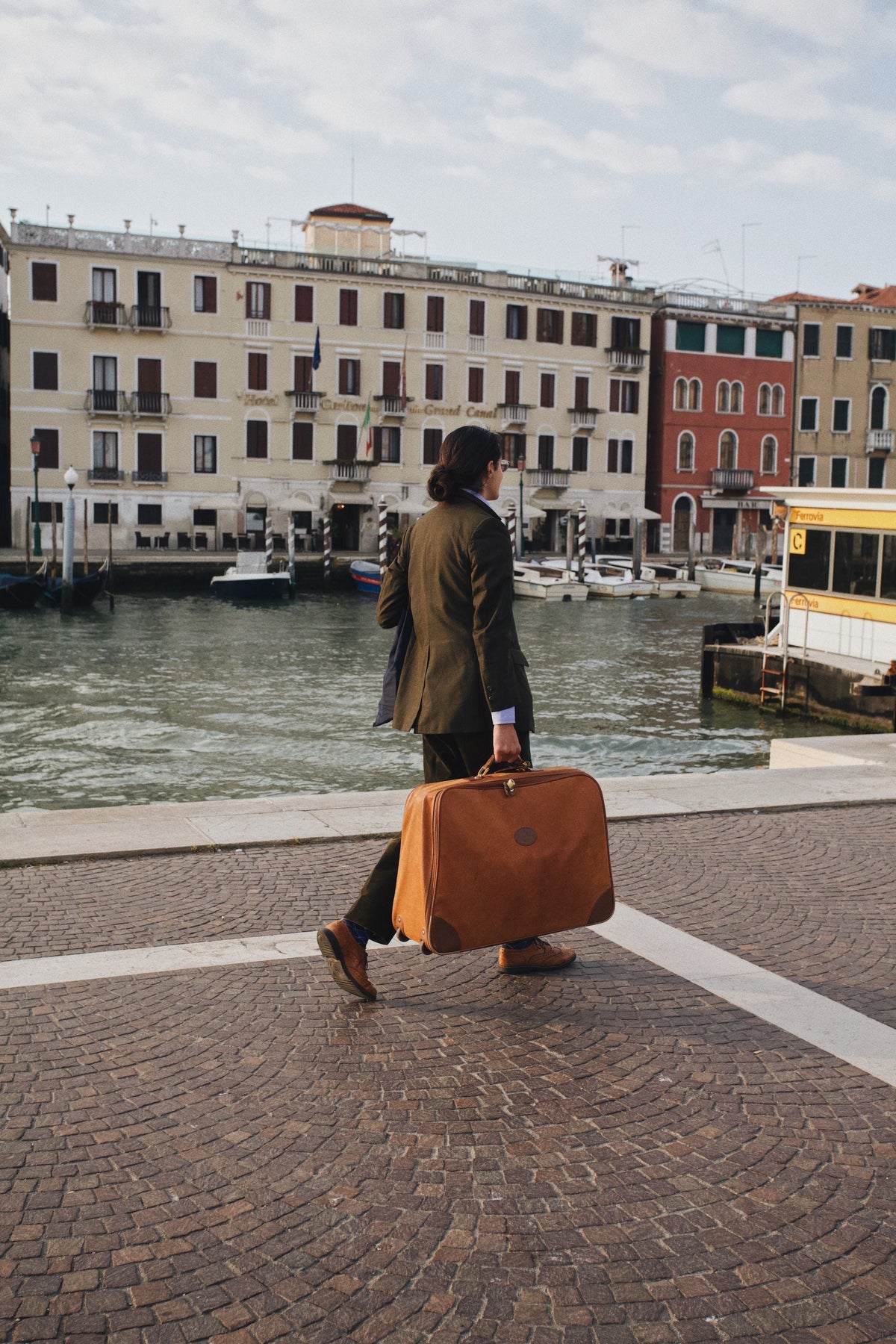 Traveler walking with a suitcase along a canal on an overcast day