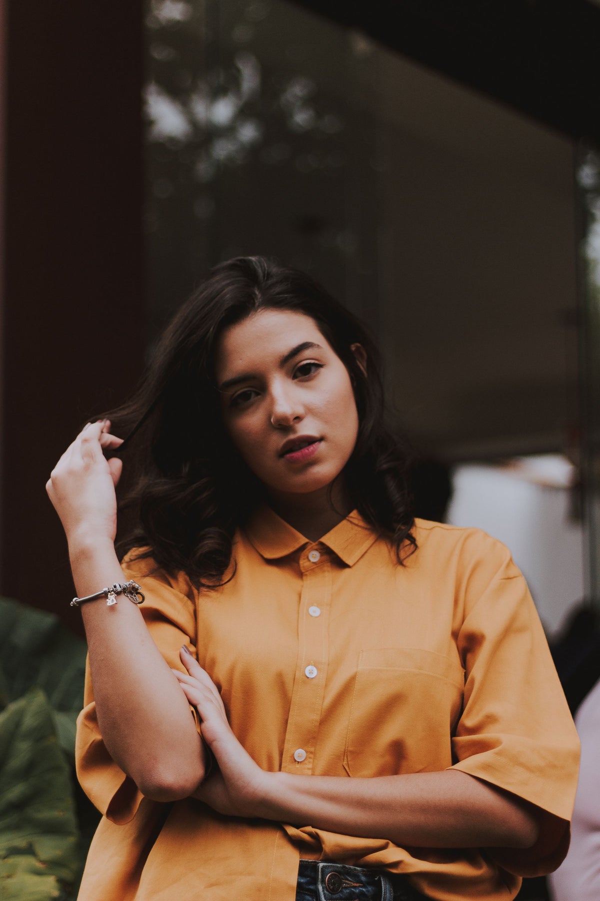 Woman wearing a mustard yellow button-up shirt posing outdoors