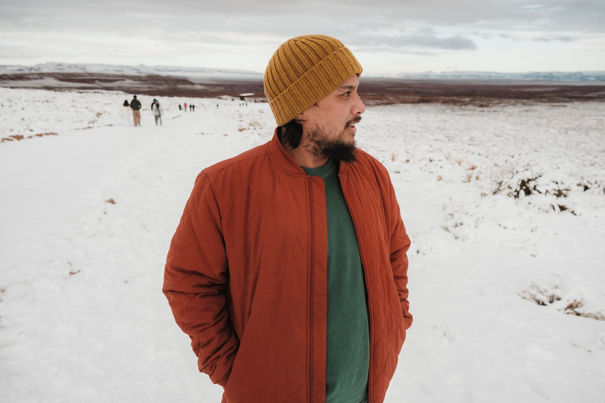 Man wearing an orange quilted coat and beanie standing in a snowy landscape