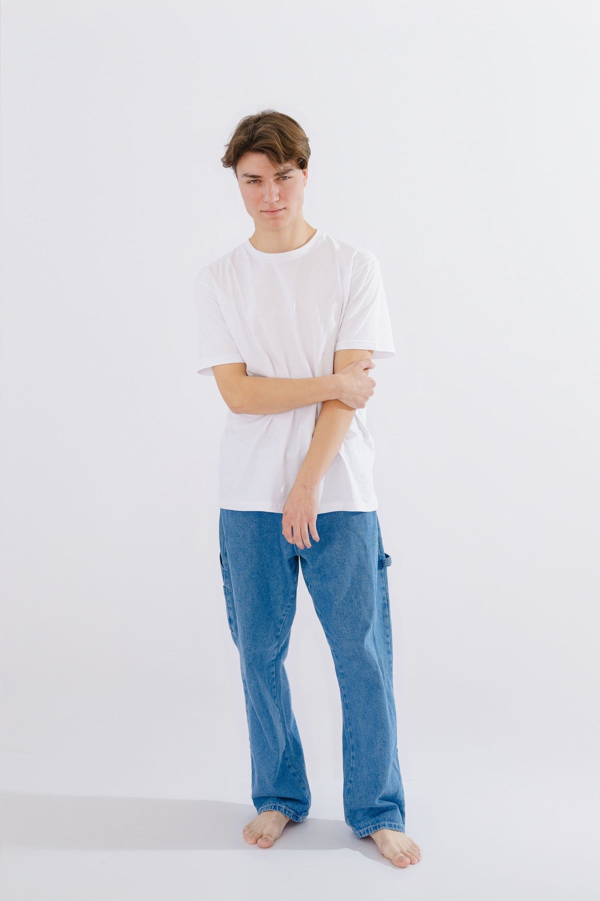 Young man in a white t-shirt and blue denim jeans standing in a studio shot