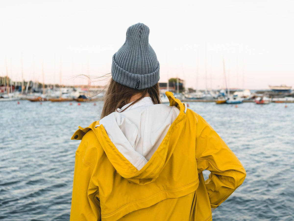 Woman wearing a yellow rain jacket looking out over a harbor with boats