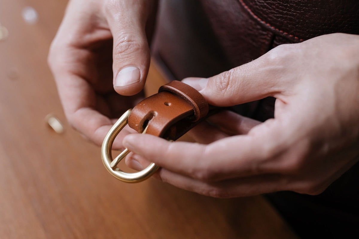 Close up of hands holding a brown leather belt buckle
