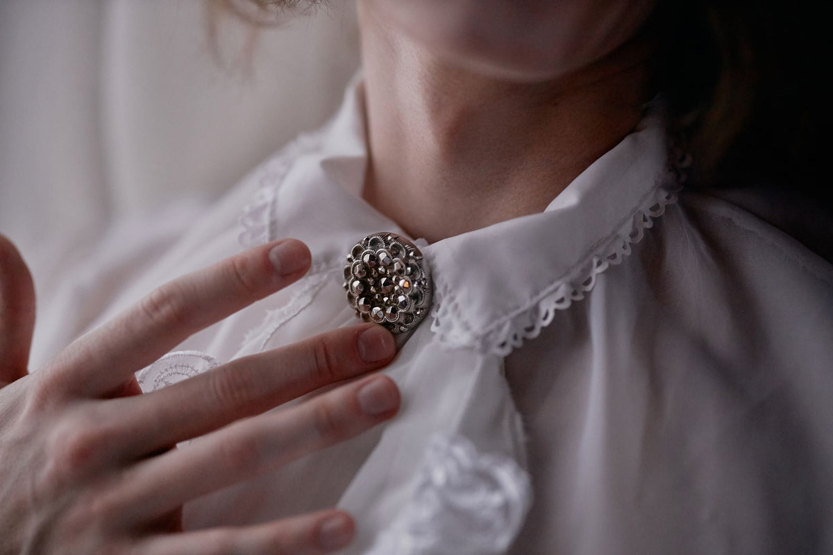 Hand touching a vintage brooch pinned to a white collar