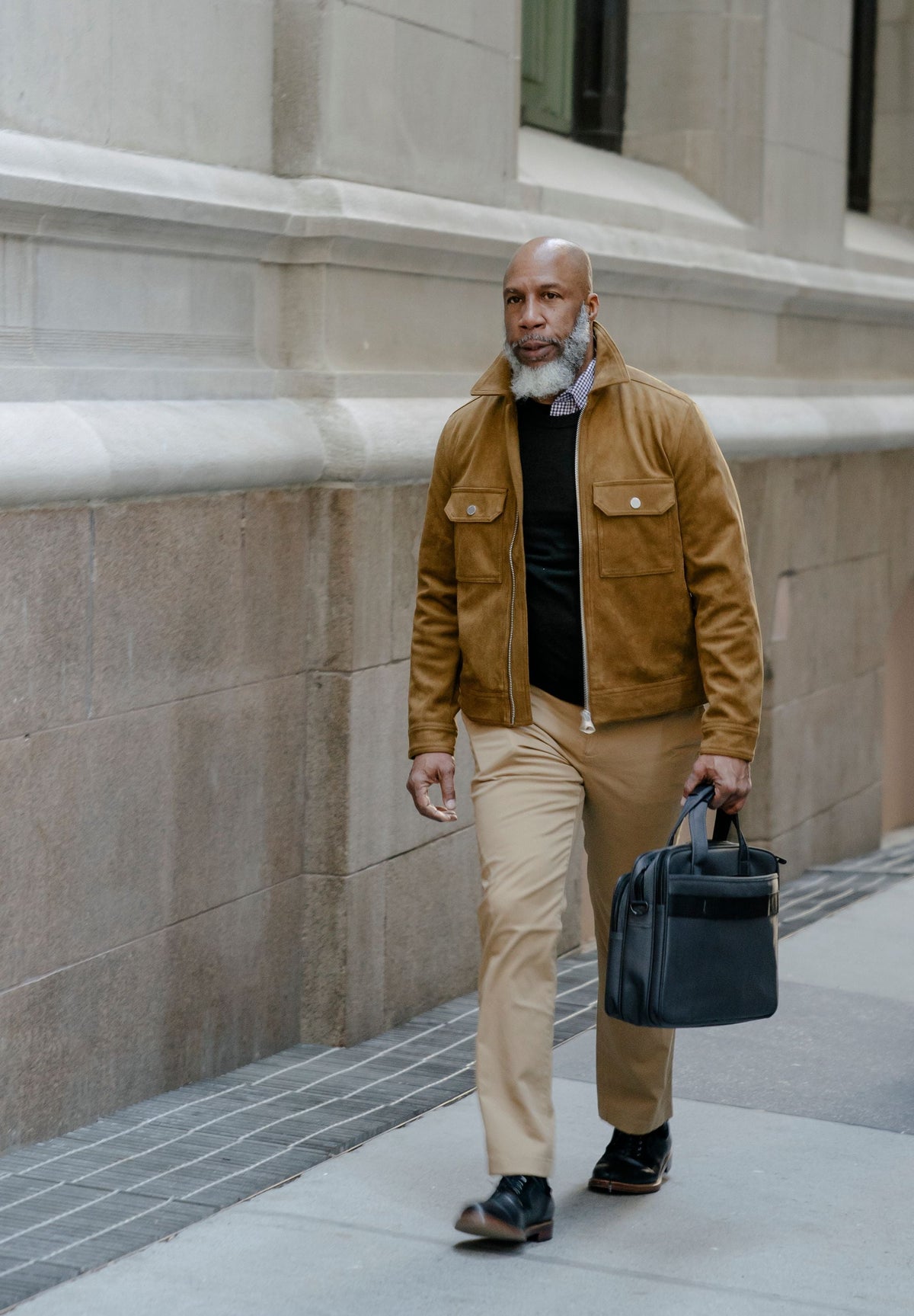 Man walking on a city sidewalk carrying a black leather briefcase, dressed in business casual attire
