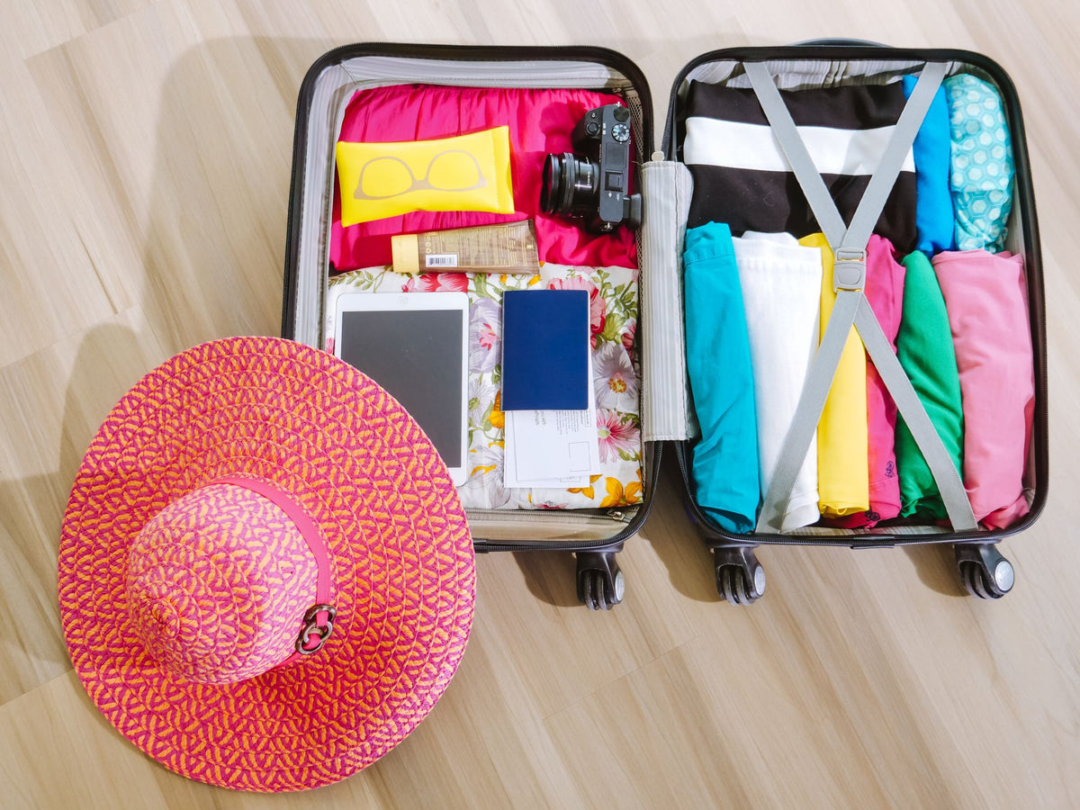 Open packed suitcase with neatly folded clothes, camera, tablet, sunglasses and a sun hat