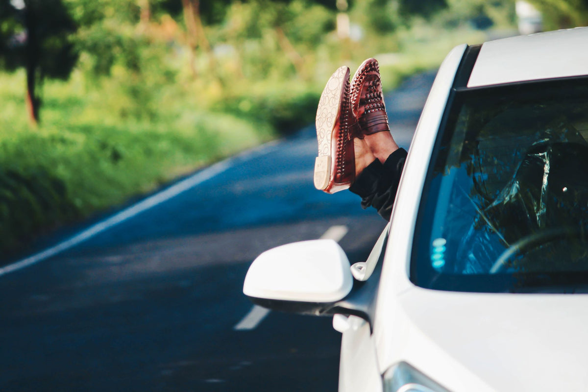 Brown leather loafers out a car window on a road trip