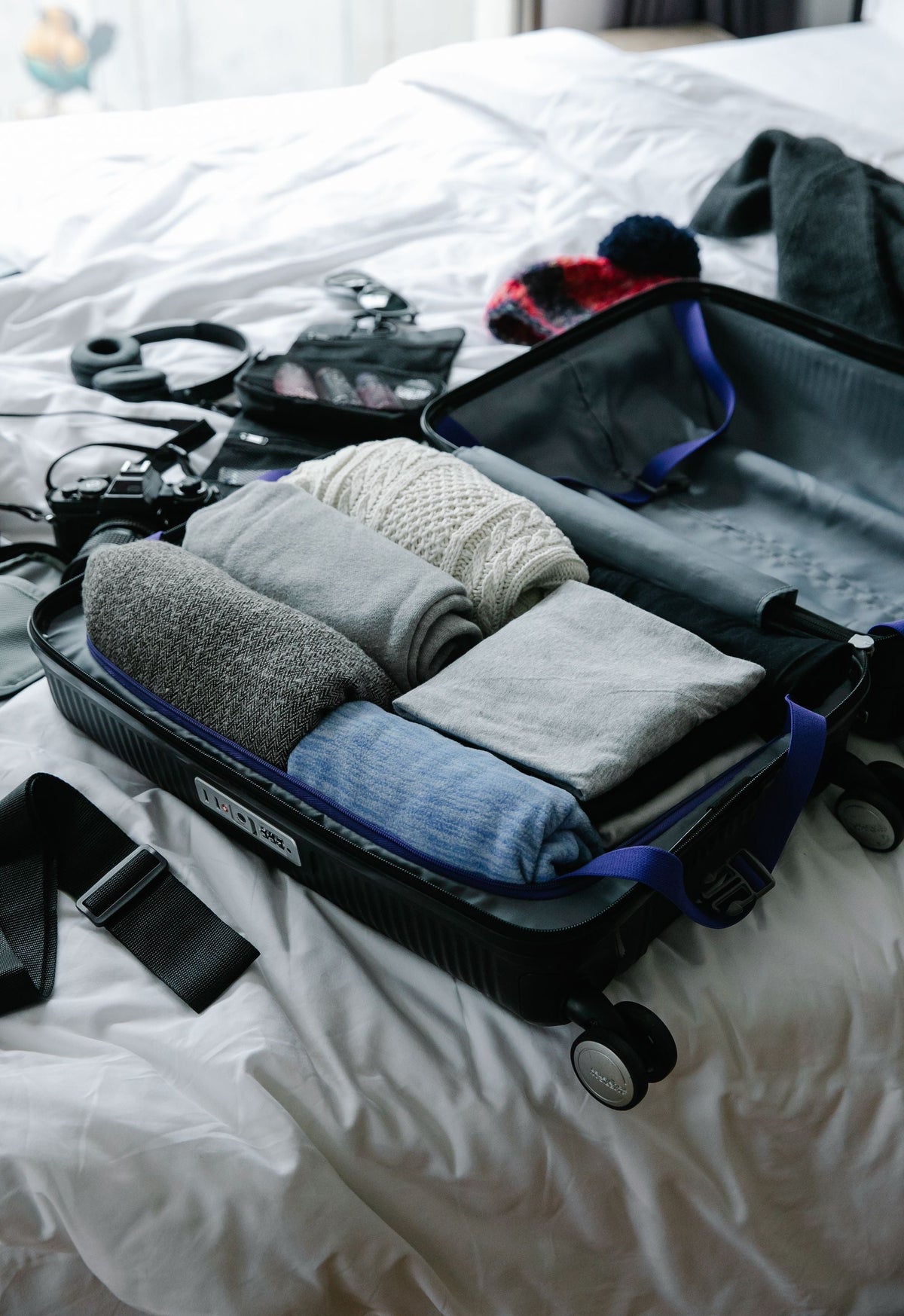 Open suitcase packed with rolled sweaters and travel essentials