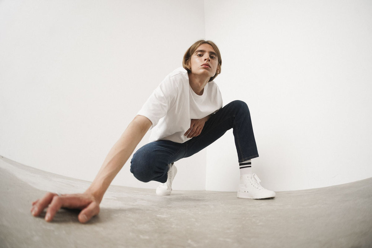 Man wearing dark denim jeans and white sneakers in studio