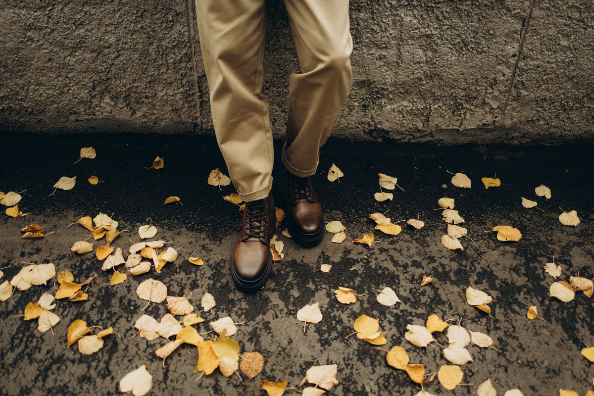 Man wearing khaki travel pants and leather boots standing on autumn leaves