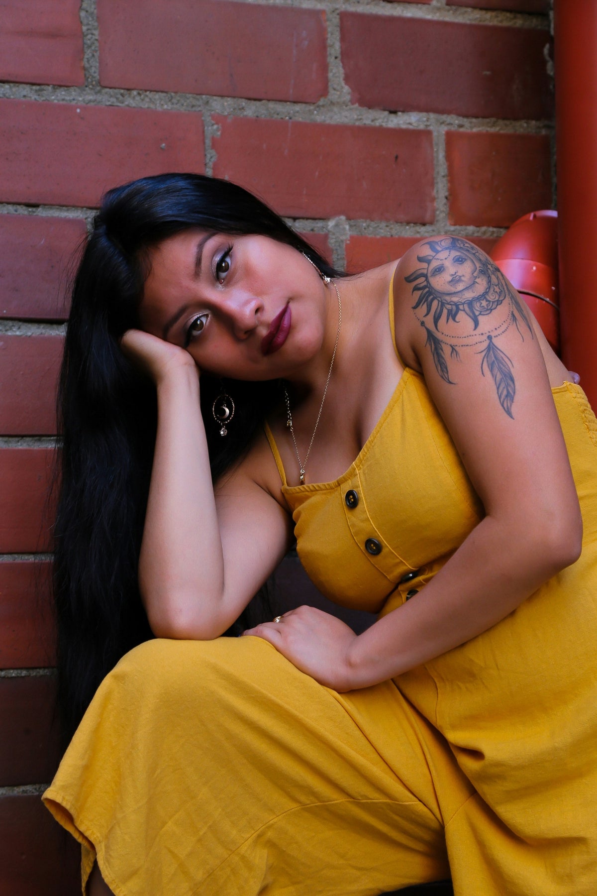 Woman wearing a yellow romper jumpsuit outdoors against a red brick wall