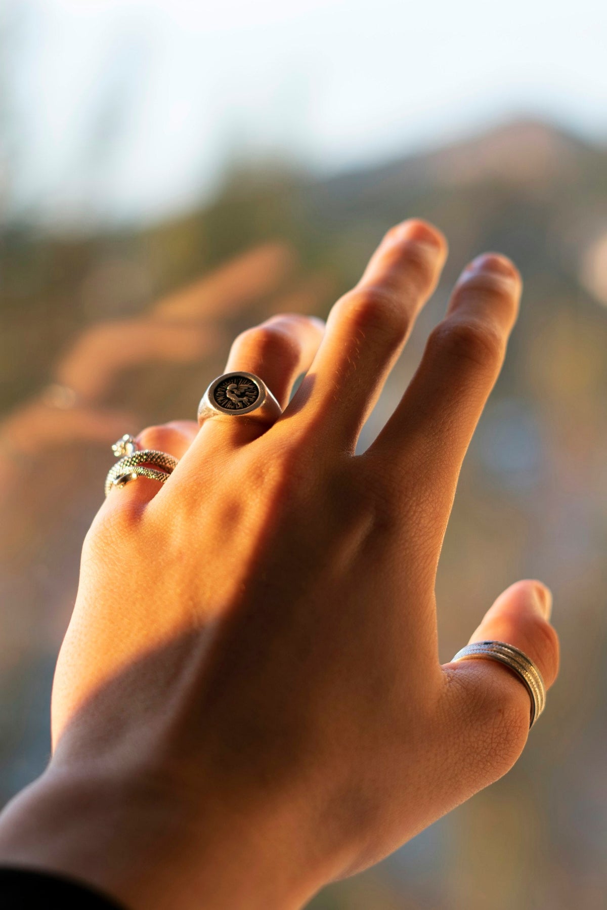 Man's hand wearing multiple stacked silver rings in warm sunset light
