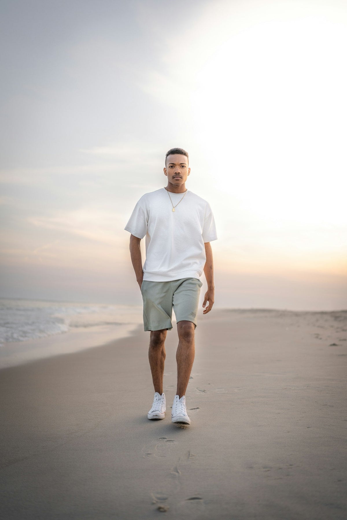 Man walking on the beach in travel shorts and a white tee at sunset