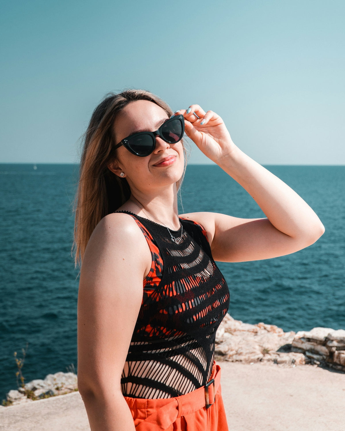 Woman wearing black sunglasses on a beach with the ocean in the background