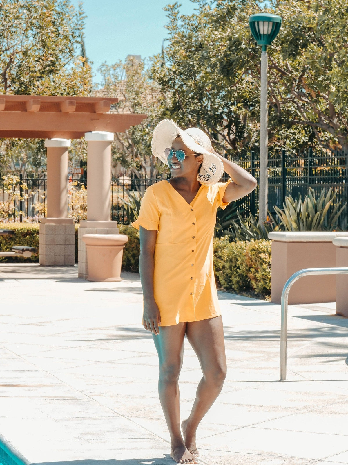 Woman in a yellow sundress and sun hat by a resort pool, dressed for a winter sun escape vacation