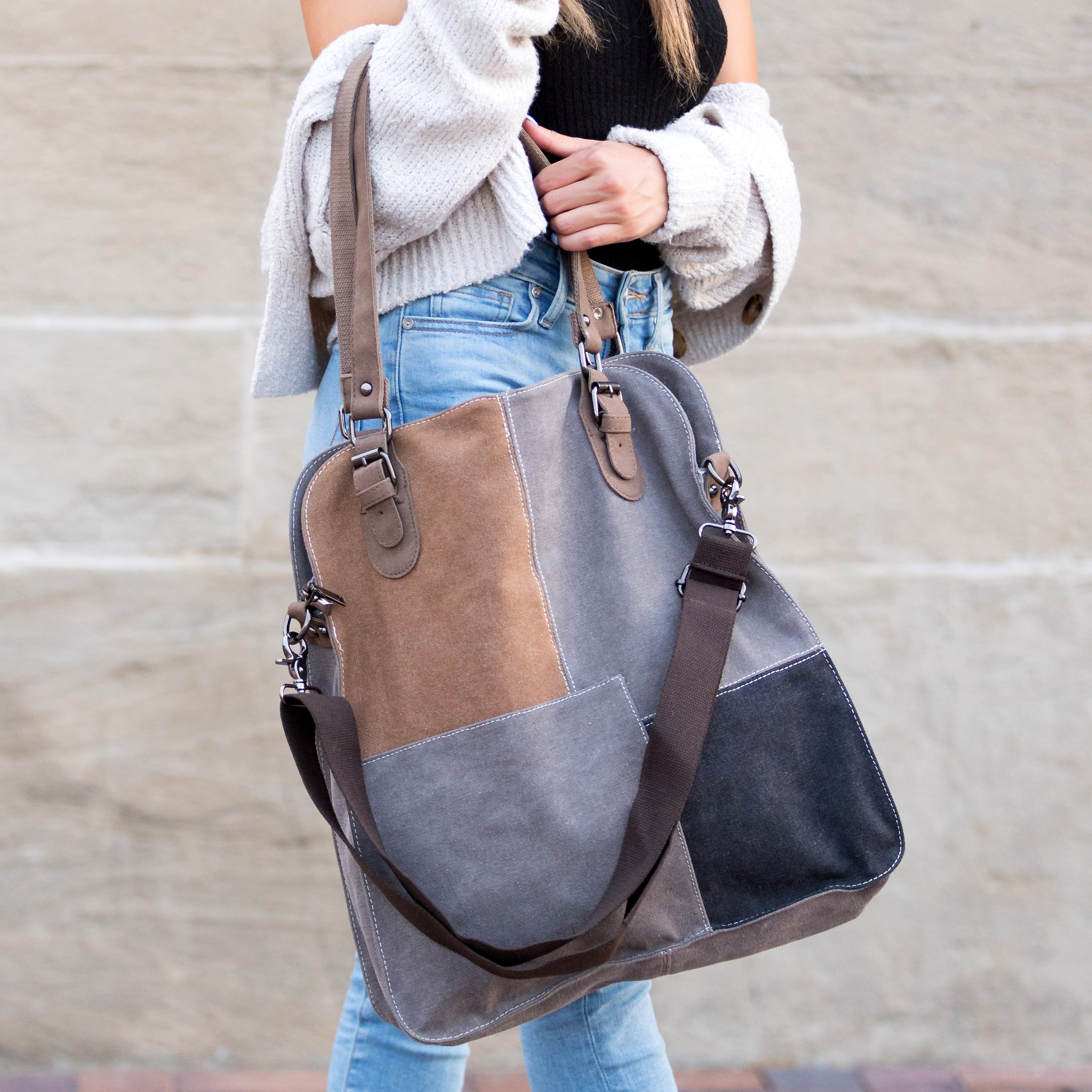 Person holding a gray and brown patchwork handbag against a neutral background