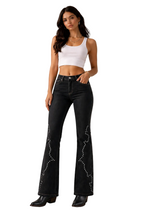 Woman wearing black flared jeans with white embellishments on a beige background