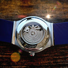 Watch with blue strap and visible mechanism on a wooden surface