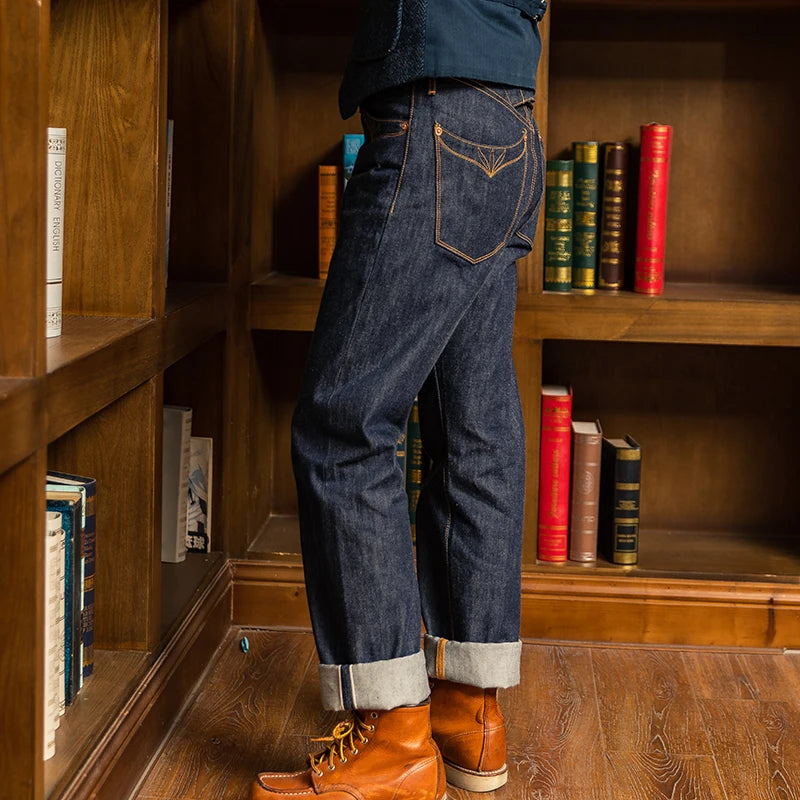 Person wearing blue jeans and brown boots standing in front of a wooden bookshelf with books.