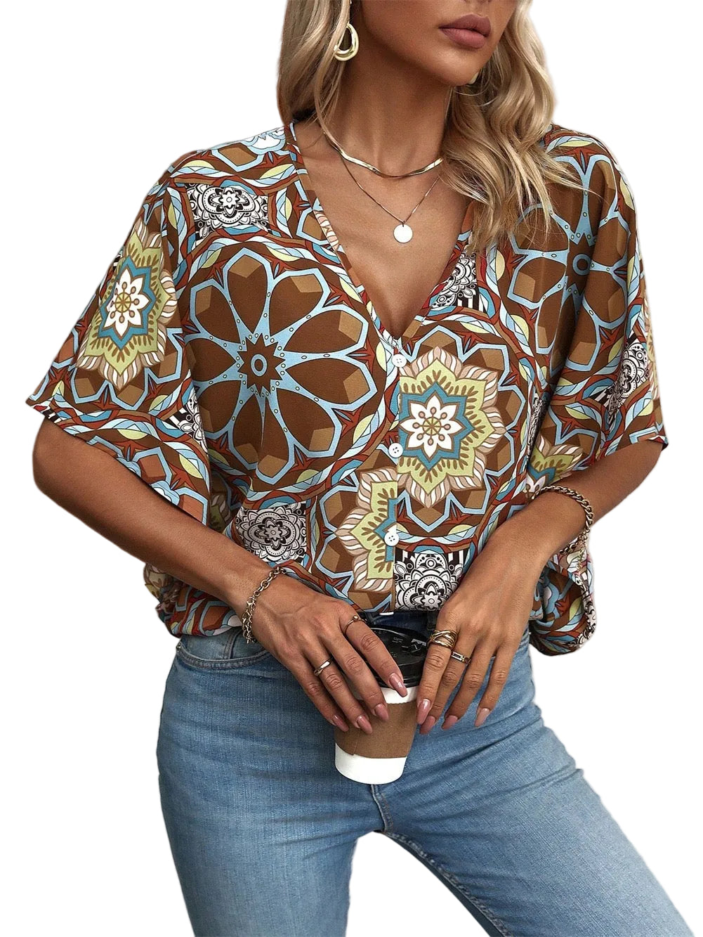 Woman wearing a patterned blouse and jeans, holding a coffee cup.