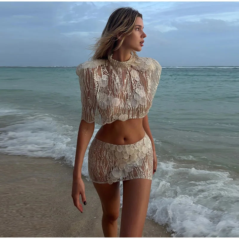 Woman in a lace outfit standing on a beach with ocean waves.