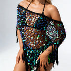 A woman wearing a black crochet off-the-shoulder cover-up with iridescent sequins in blue, green, and purple, set against a plain white studio background.