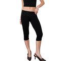 A model wearing black capri leggings with a white polka-dot patterned waistband, paired with a matching black polka-dot crop top and black slingback heels, standing in a room with a wooden floor and a pink chair.