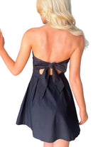 Woman wearing a black dress with a bow detail, standing in a room.