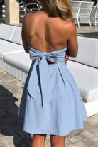 Woman wearing a light blue dress with a bow detail in an outdoor setting.