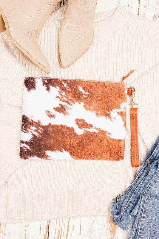 Aili's Corner animal print clutch bag in brown and white fur placed on a beige sweater with boots