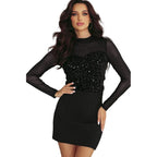 YNIQUE model wearing black holiday party sequin blouse with sheer long sleeves and fitted black mini skirt by Christmas tree