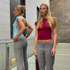 Two women wearing backless clubwear slim fit tops in blue and red paired with gray pants indoors