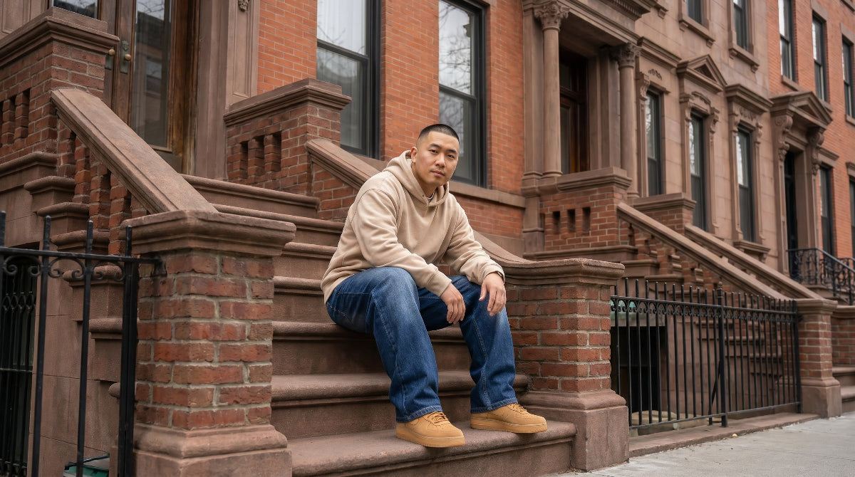 Man wearing dark blue wide-leg baggy jeans seated on Brooklyn brownstone stoop, cinematic landscape view