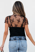 Back view of woman wearing YNIQUE black floral sheer mesh blouse over camisole with light wash jeans