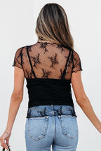 Back view of woman wearing YNIQUE black floral sheer mesh blouse over camisole with light wash jeans