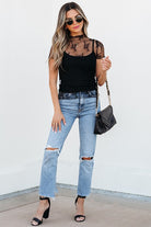 YNIQUE model wearing a black cami layered under a floral sheer mesh blouse with ripped jeans and black heels