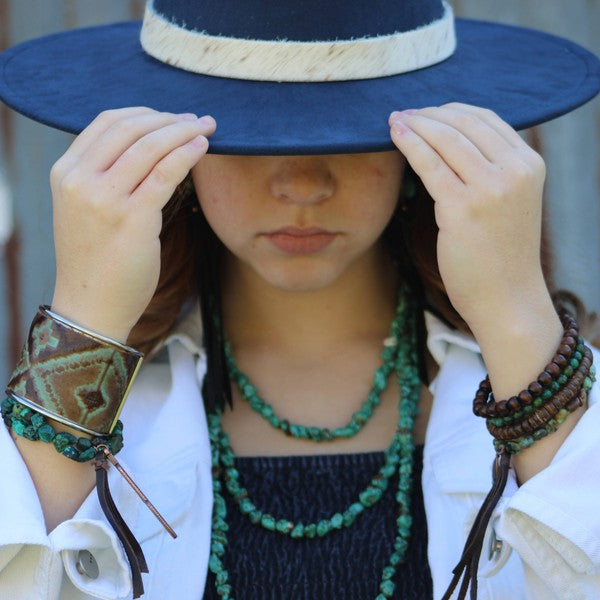 Model wearing multiple bracelets including a black african turquoise bead bracelet and a wide-brimmed hat
