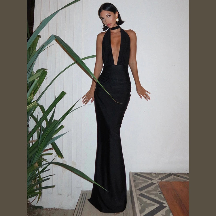 Woman wearing a black halter deep v neck maxi dress standing indoors near a plant