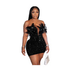 Woman wearing a black sequin feather mini dress standing in front of an ornate mirror holding a silver handbag