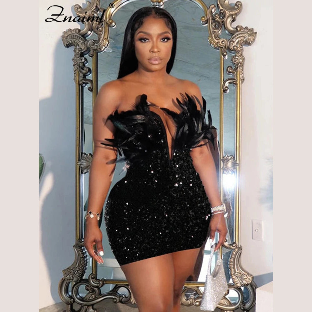 Woman wearing a black sequin feather mini dress standing in front of an ornate mirror holding a silver handbag