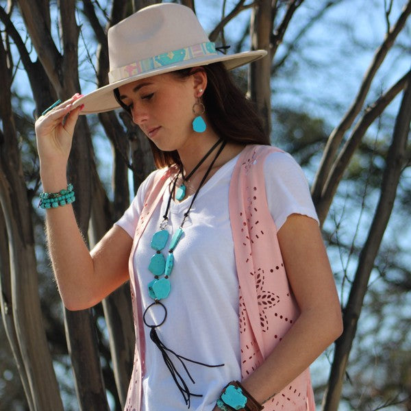 A woman wearing blue turquoise chunky earrings with matching jewelry and a wide-brim hat outdoors