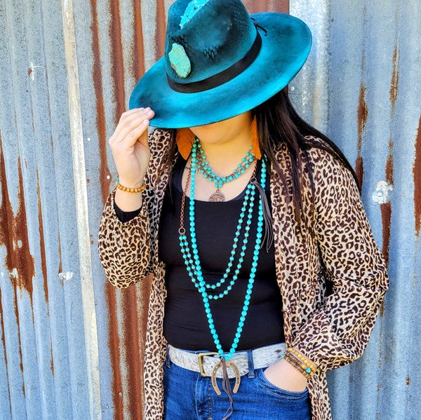 Fashionable woman wearing a blue turquoise coin necklace with a leopard print jacket and wide-brim hat