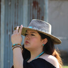 Woman wearing blue turquoise stud earrings and a stylish hat in a rustic outdoor setting