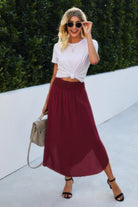 Woman wearing a boho print flowy skirt in deep red paired with a white knotted top and black sandals