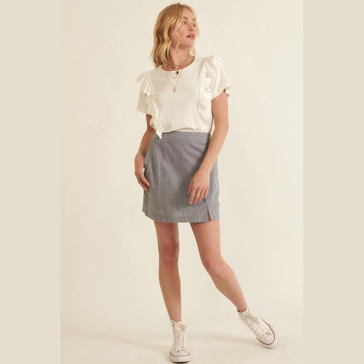 Woman wearing a chic pinstripe skirt for women paired with white ruffle sleeve top and sneakers