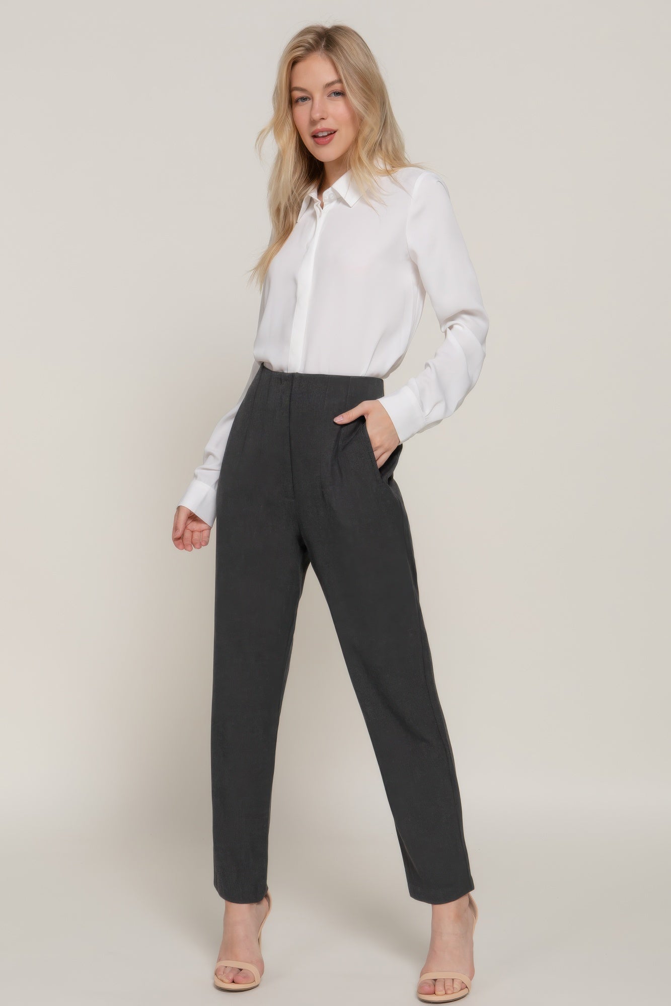Woman wearing stylish high rise trousers in dark gray with a white blouse and sandals
