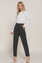 Woman wearing stylish high rise trousers in dark gray with a white blouse and sandals