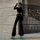 Woman wearing sheer streetwear crop tee for women with long sleeves and cutout shoulders paired with black pants and green heels