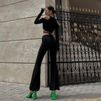 Woman wearing sheer streetwear crop tee for women with long sleeves and cutout shoulders paired with black pants and green heels